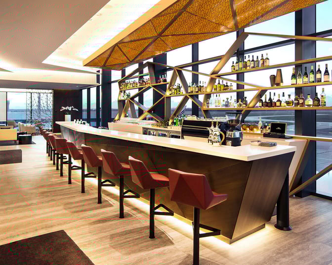 The bar at The House by Aspire in Melbourne Airport features a counter with seating and a selection of displayed spirits.