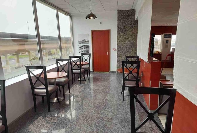 The seating area in the Air France Lounge at Douala International Airport features tables and chairs with views of the tarmac.