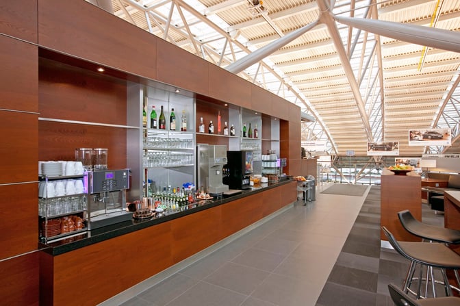 The bar area in Hamburg Airport Lounge features a selection of spirits, glassware, and a coffee machine for guests.