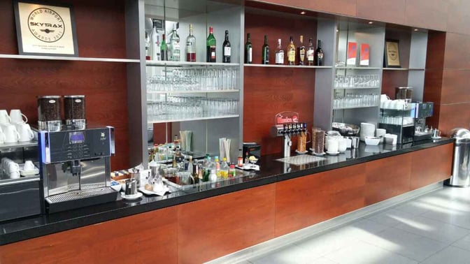 The bar area at Hamburg Airport Lounge features a self-serve coffee machine, beverage dispensers, and a selection of spirits and glassware.