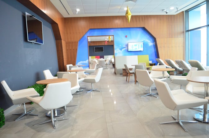 The seating area at Akwaaba Lounge in Kotoka International Airport features comfortable chairs and tables with a view of flight information screens.