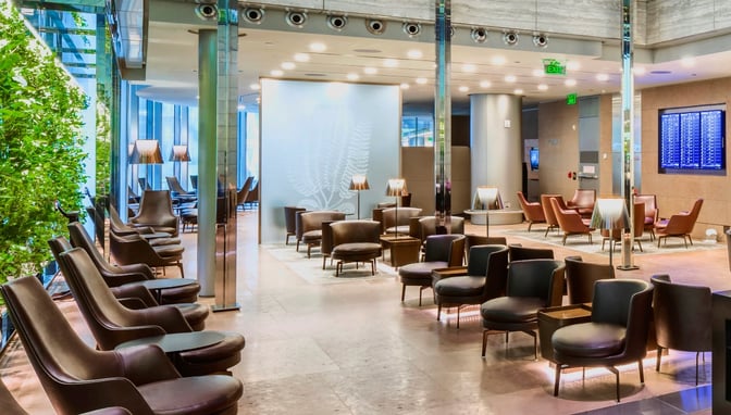 The Al Maha Lounge at Doha Hamad International Airport features a seating area with armchairs, side tables, and a flight information display.