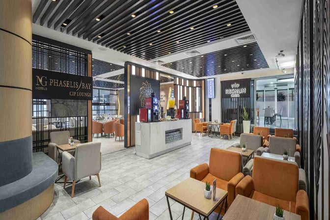 The CIP Lounge at Antalya Airport features a seating area with tables and chairs, and a self-serve beverage station.