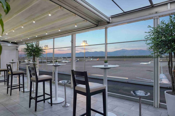 The CIP Lounge at Antalya Airport features high-top tables and chairs with expansive views of the runway and surrounding mountains.