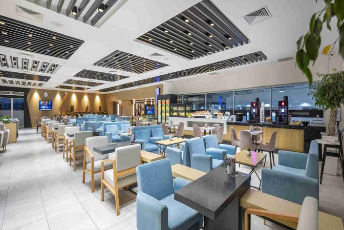 The CIP Lounge at Antalya Airport features a spacious seating area with armchairs and tables, adjacent to a self-serve food station.