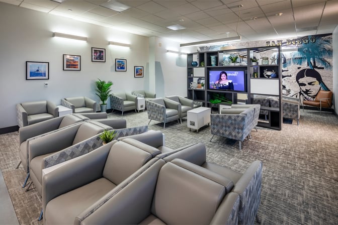 The Aspire Lounge at San Diego International Airport features comfortable seating with a television and decorative wall art.