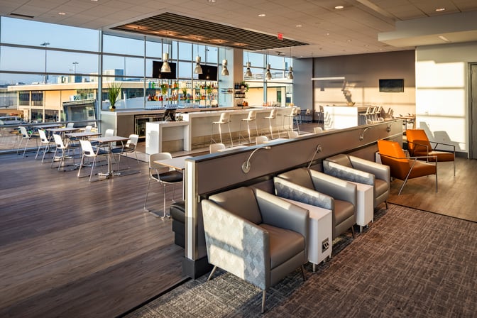 The Aspire Lounge at San Diego International Airport features a bar with seating and tables offering views of the tarmac.