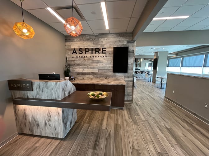 The Aspire Lounge entrance at Ontario International Airport features a reception desk and leads to a seating area with tables.