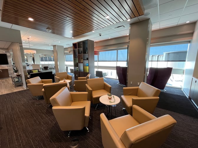 The Aspire Lounge at Ontario International Airport features comfortable seating with armchairs and small tables, offering views of the tarmac.