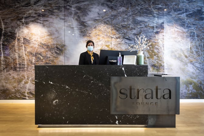 The reception desk at Strata Lounge, Auckland Airport, features a staff member ready to assist guests with check-in.