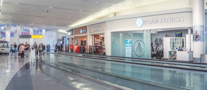 The ROAM Fitness entrance at Baltimore-Washington International Airport offers workout gear and showers, located near a moving walkway.
