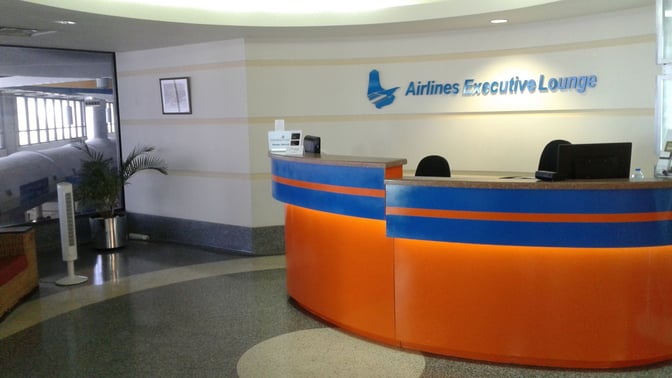 The reception area of the Airlines Executive Lounge at Grantley Adams International Airport features a curved desk and seating for guests.