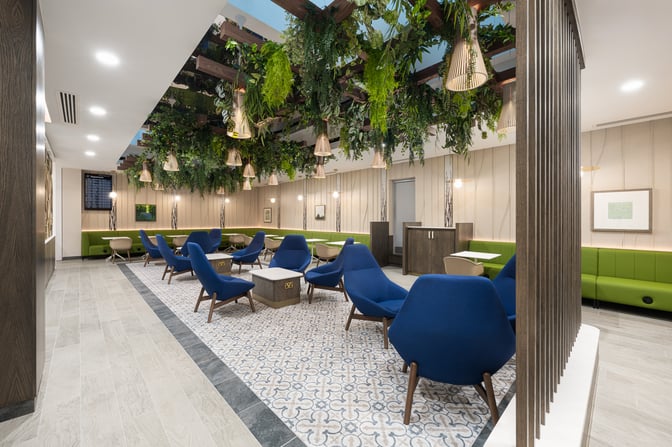 The Essence Lounge at Bristol Airport features seating with armchairs and tables, surrounded by greenery and clean overhead lighting.