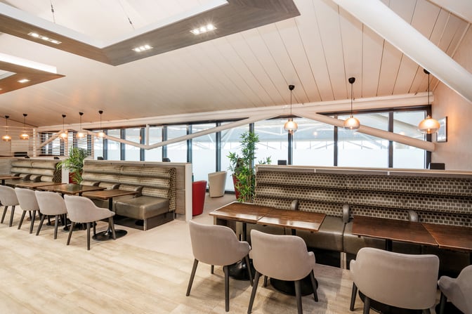Booth seating at Bristol Airport's Essence Lounge offers semi-private spaces with tables and chairs, adjacent to large windows.