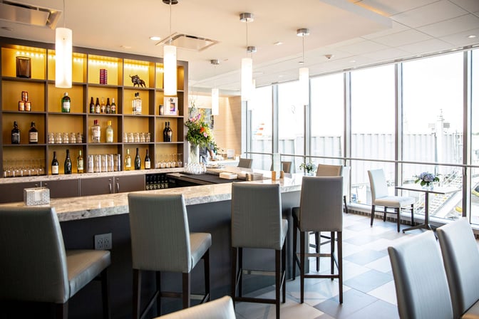 The Club BUF at Buffalo Niagara International Airport features a bar with a selection of spirits and seating overlooking the tarmac.