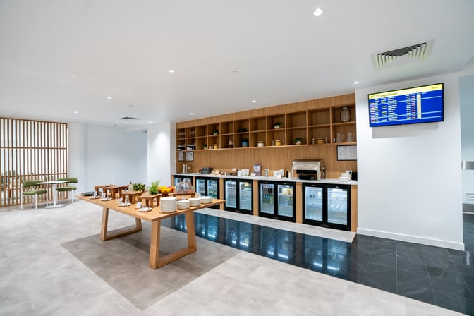 The Escape Lounge at Cairns Airport features a self-serve food area with beverages, snacks, and a flight information display.