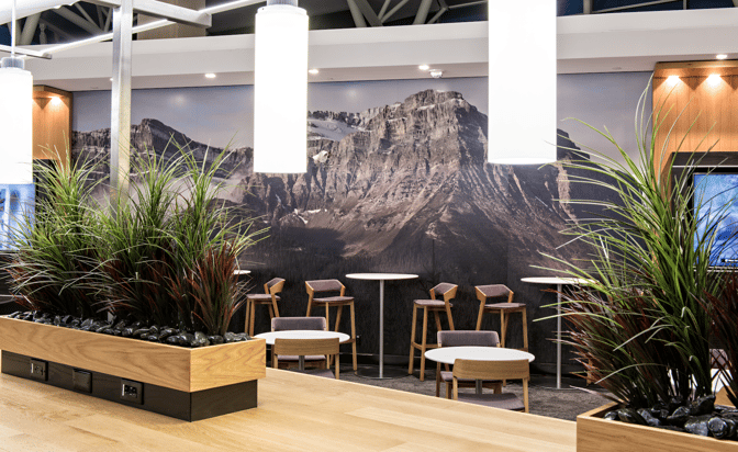 The Aspire Lounge at Calgary International Airport features a seating area with tables and chairs, complemented by decorative plants.
