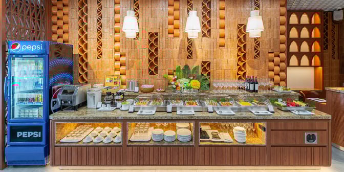 The SH Premium Lounge at Cam Ranh International Airport features a buffet with a variety of dishes, beverages, and a drink cooler.