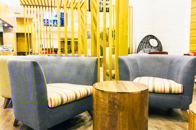 Seating area in the MERA Business Lounge at Cancun International Airport features cushioned chairs and a wooden table for passenger comfort.