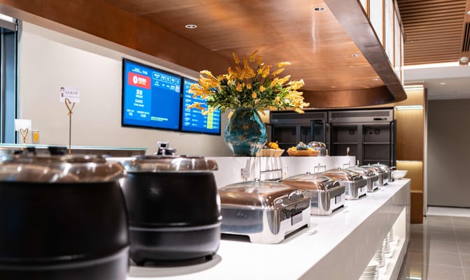 Buffet area in First Class Lounge 2 at Chengdu Shuangliu International Airport features self-serve hot dishes and flight information screens.