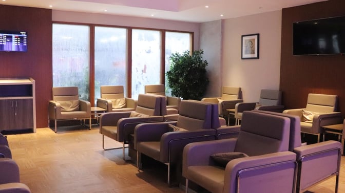 The seating area in Travel Club Lounge A at Chennai International Airport features armchairs, a flight information screen, and a television.