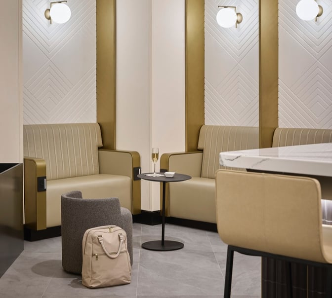The seating area in The Club MDW features comfortable chairs, a small table with a drink, and a nearby bag.