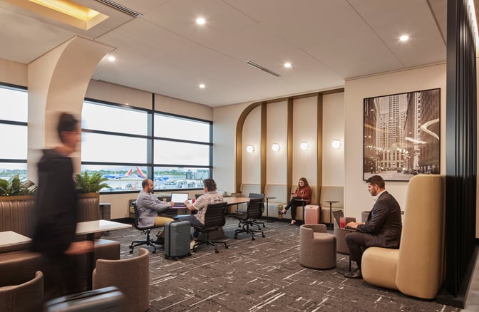 The seating area at The Club MDW features tables and chairs with views of the airport runway through large windows.