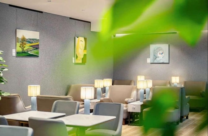 The seating area in Plaza Premium Lounge at Chongqing Airport features comfortable chairs, tables, and lamps, with artwork on the walls.