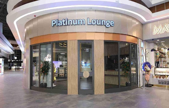 The entrance to the Platinum Lounge at Cukurova International Airport features glass doors and is located near retail shops.