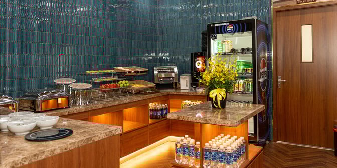 Self-serve food and beverage area in SH Premium Lounge Da Nang offers snacks, drinks, and fresh fruit for travelers.