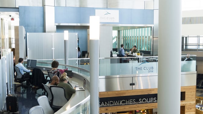 The Club DFW at Dallas-Fort Worth International Airport features a seating area with workstations and a bar serving guests.