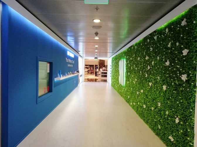 The entrance to Be Relax Lounge at Doha Hamad International Airport features a green wall and leads to a retail area.