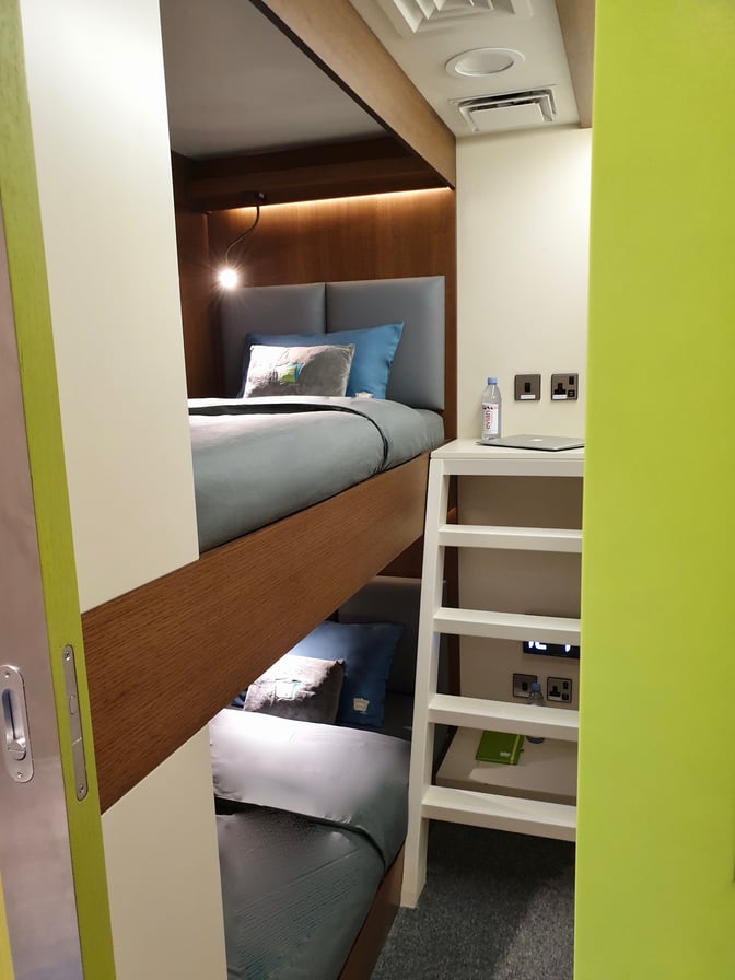The sleep 'n fly YAWN Bunk Cabin at Doha Hamad International Airport features bunk beds for two adults with a small table and power outlets.