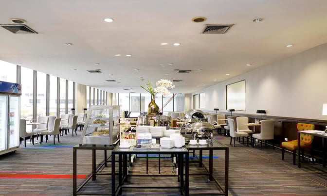 The Miracle Lounge at Don Mueang International Airport features a self-serve buffet area with seating and views of the tarmac.