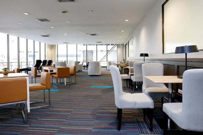 The seating area in Miracle Lounge at Don Mueang International Airport features tables with chairs and armchairs, offering airport views.