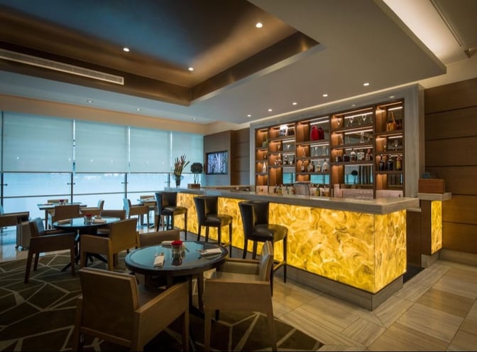 The Ahlan Business Class Lounge at Dubai International Airport Concourse D features a bar with seating and a variety of displayed beverages.