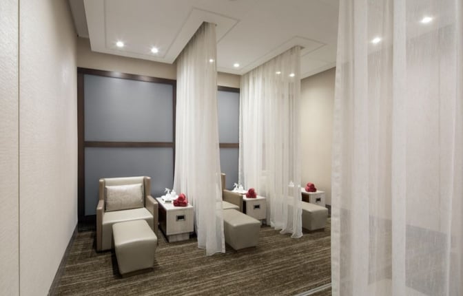 Semi-private relaxation area in the Ahlan First Class Lounge features comfortable seating with footrests, separated by sheer curtains for privacy.