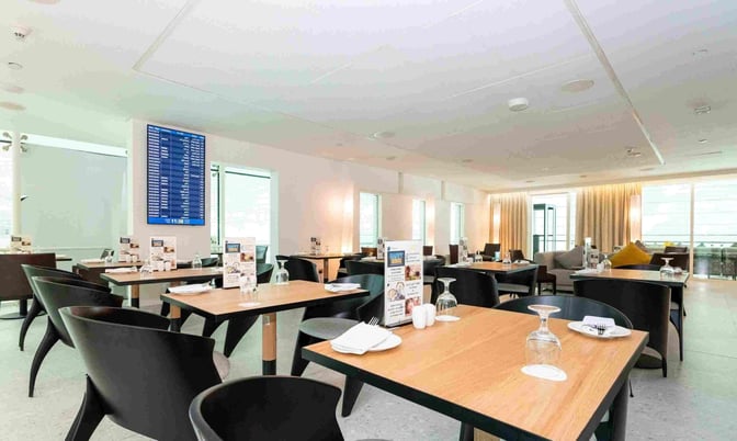 The Ahlan Lounge at Gate A1 in Dubai International Airport features dining tables with place settings and a visible flight information screen.