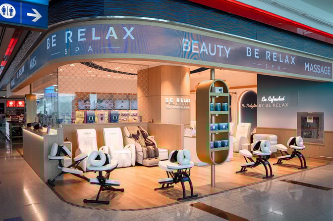 The Be Relax Spa A23 at Dubai International Airport offers massage chairs and wellness products near the seating area for travelers.