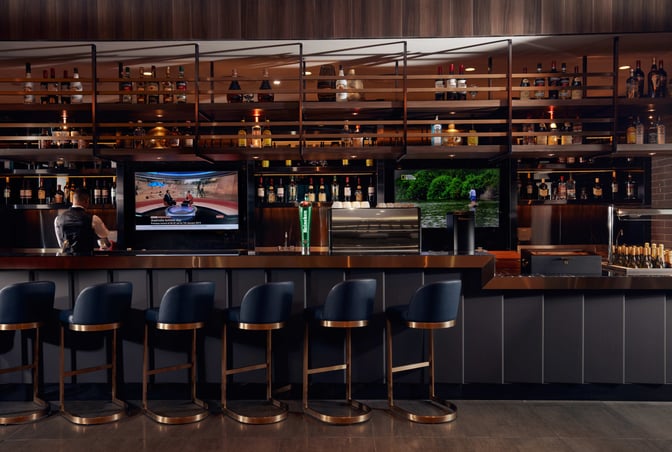 The bar at Plaza Premium Lounge in Dubai International Airport offers a selection of spirits and features counter seating with televisions.