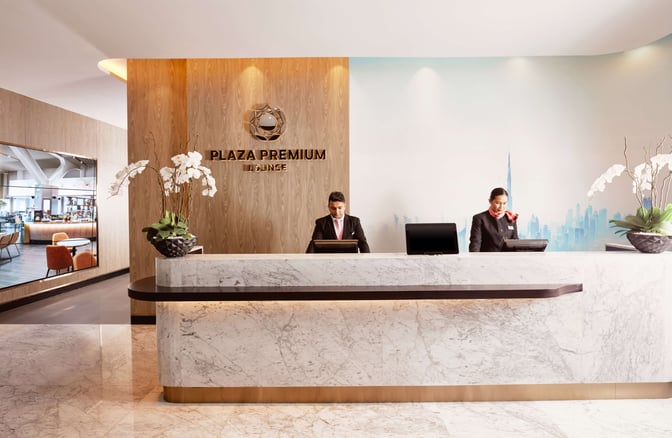 The reception area of Plaza Premium Lounge at Dubai International Airport features a marble counter with staff ready to assist travelers.