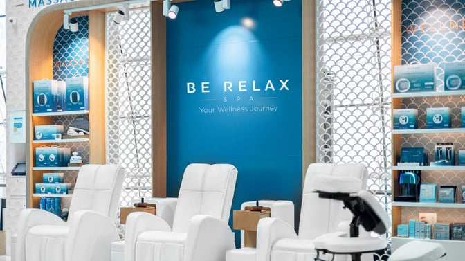 The Be Relax Spa B13 at Dubai International Airport features massage chairs and shelves displaying wellness products for travelers.