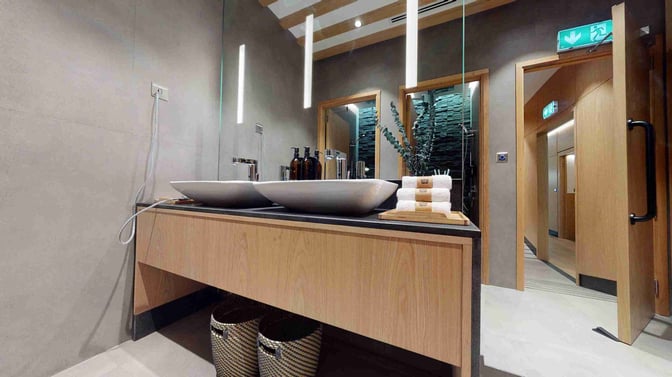 The Sleepover Lounge at Dubai International Airport Concourse B features a washroom area with dual sinks, toiletries, and neatly stacked towels.