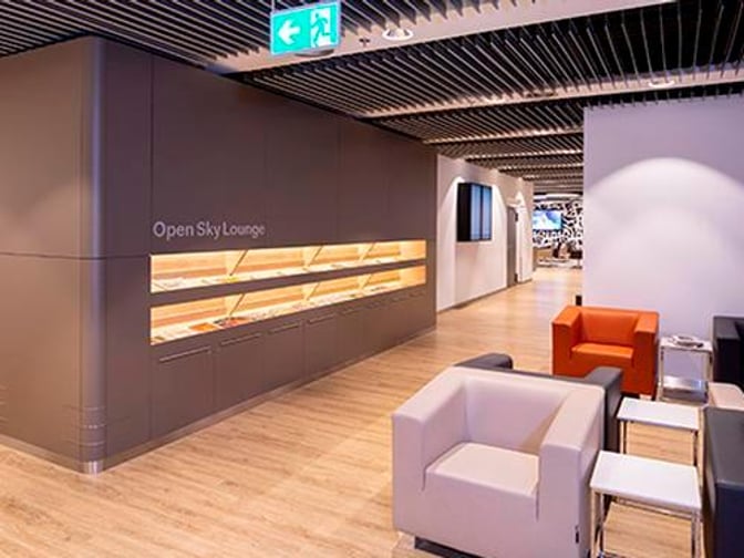 The Open Sky Lounge at Dusseldorf Airport features a seating area with armchairs and a display wall for reading materials.