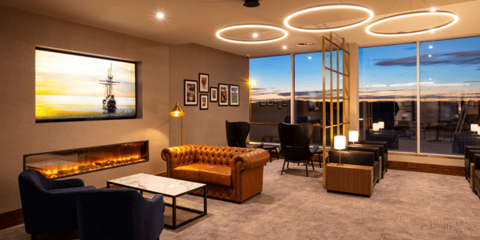 The seating area in Plaza Premium Lounge at Edinburgh Airport features comfortable chairs, a sofa, and a digital fireplace with airport views.
