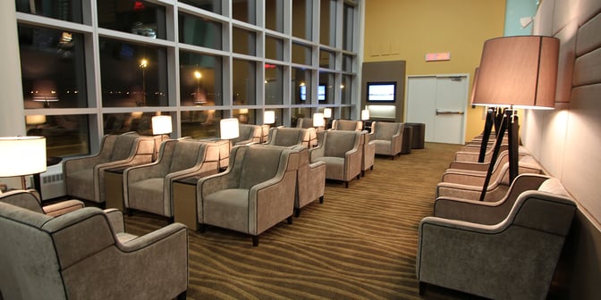The seating area at Plaza Premium Lounge, Edmonton International Airport, features armchairs with individual lamps and large windows overlooking the tarmac.