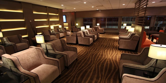 The seating area in Plaza Premium Lounge at Edmonton International Airport features comfortable armchairs with side tables and ambient lighting.