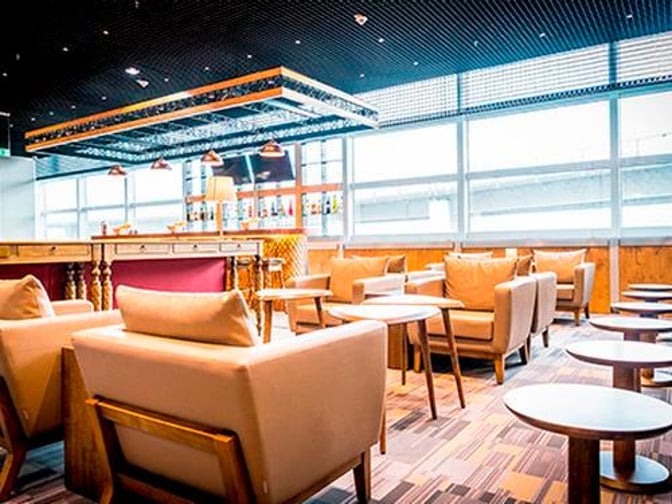 The Primeclass Lounge at Frankfurt Airport features a seating area with armchairs and tables, adjacent to a bar with various beverages.