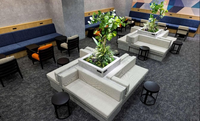 The seating area in the Lounge TIME/International at Fukuoka Airport features cushioned benches, small tables, and central planters for relaxation.