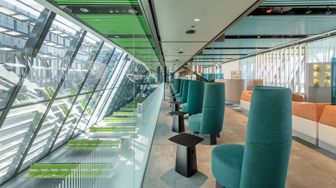 The Crystal Lounge at Geneva International Airport features high-backed seating with individual tables, offering views of the terminal through large glass windows.